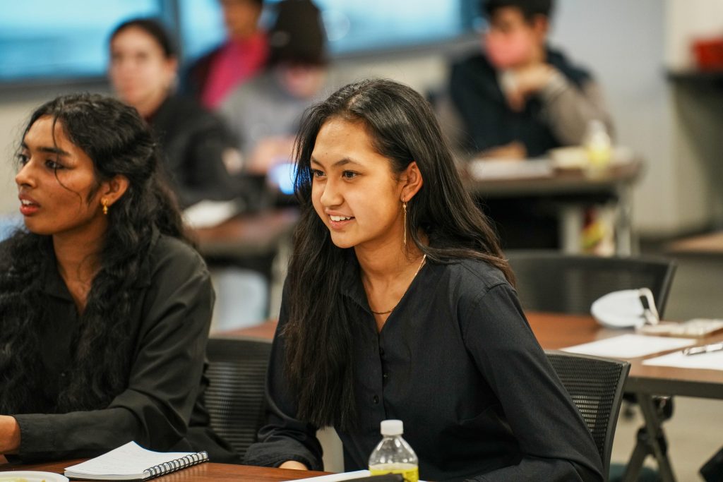 Sarada Gundavarapu and Micky Nguyen, founders of the Future Medical Professionals Club, are high school females with long hair and are sitting at a table facing the speakers at the front of the room during the UCHealth Panel. 