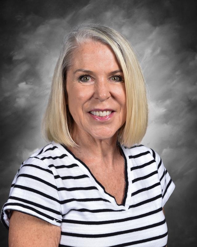 A smiling woman with shoulder-length blonde hair, wearing a striped shirt, against a gray background.